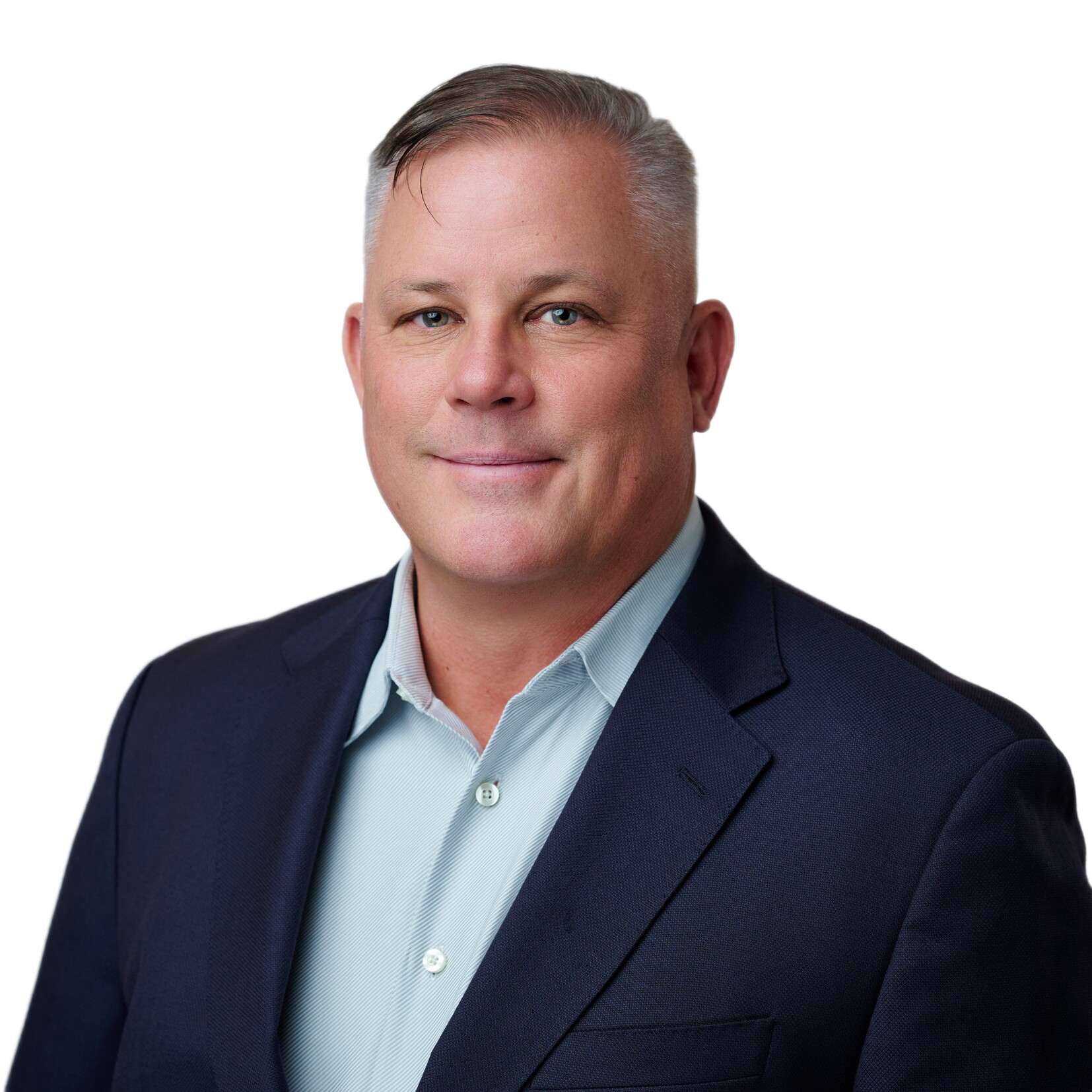 A man with short gray hair wearing a dark suit jacket and light blue dress shirt poses against a plain white background.