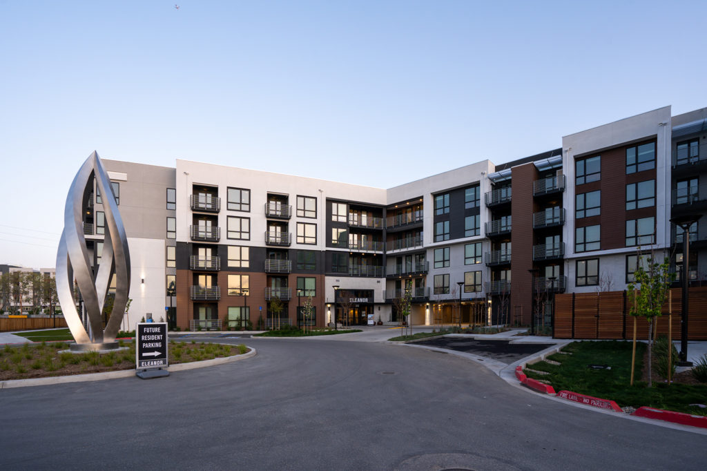 Modern apartment complex with white, black and brown exterior and a circle drive and large metal sculpture in the middle