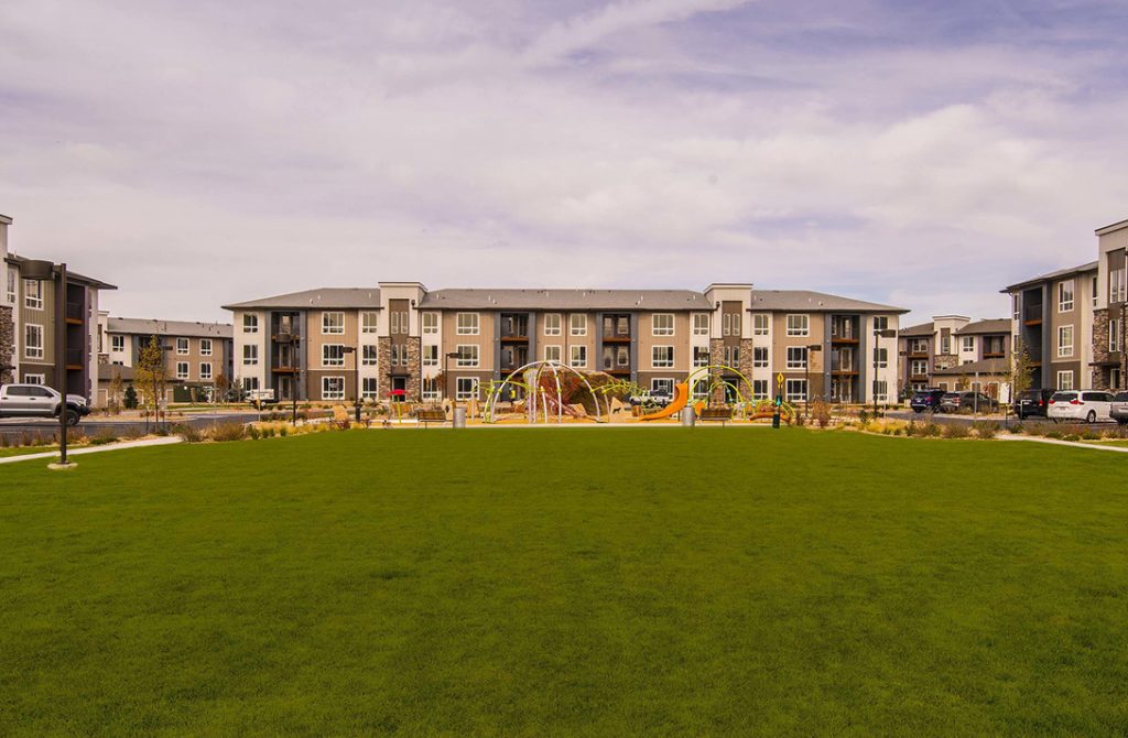 Shot of brown and white apartment buildings across a green field with a play area in the middle