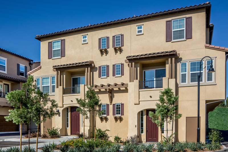 Three-story yellow-brown townhouses with dark brown roofing, shutters and doors with small balconies and little trees out front