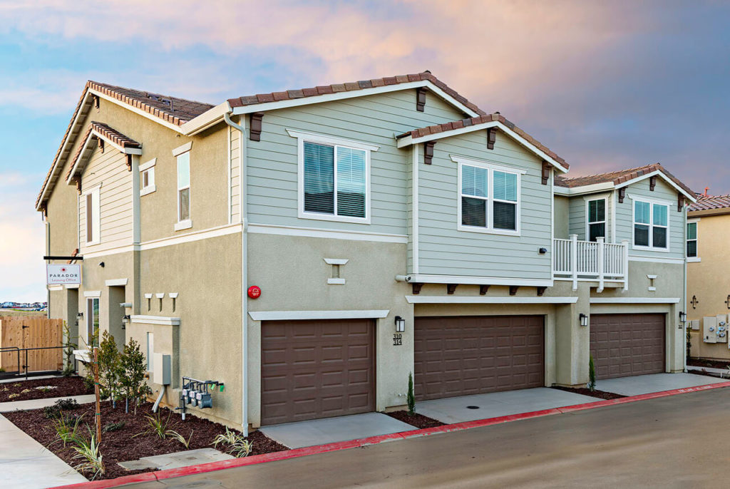 Sage green two story townhouses with white windows and brown garage doors on a sunset sky