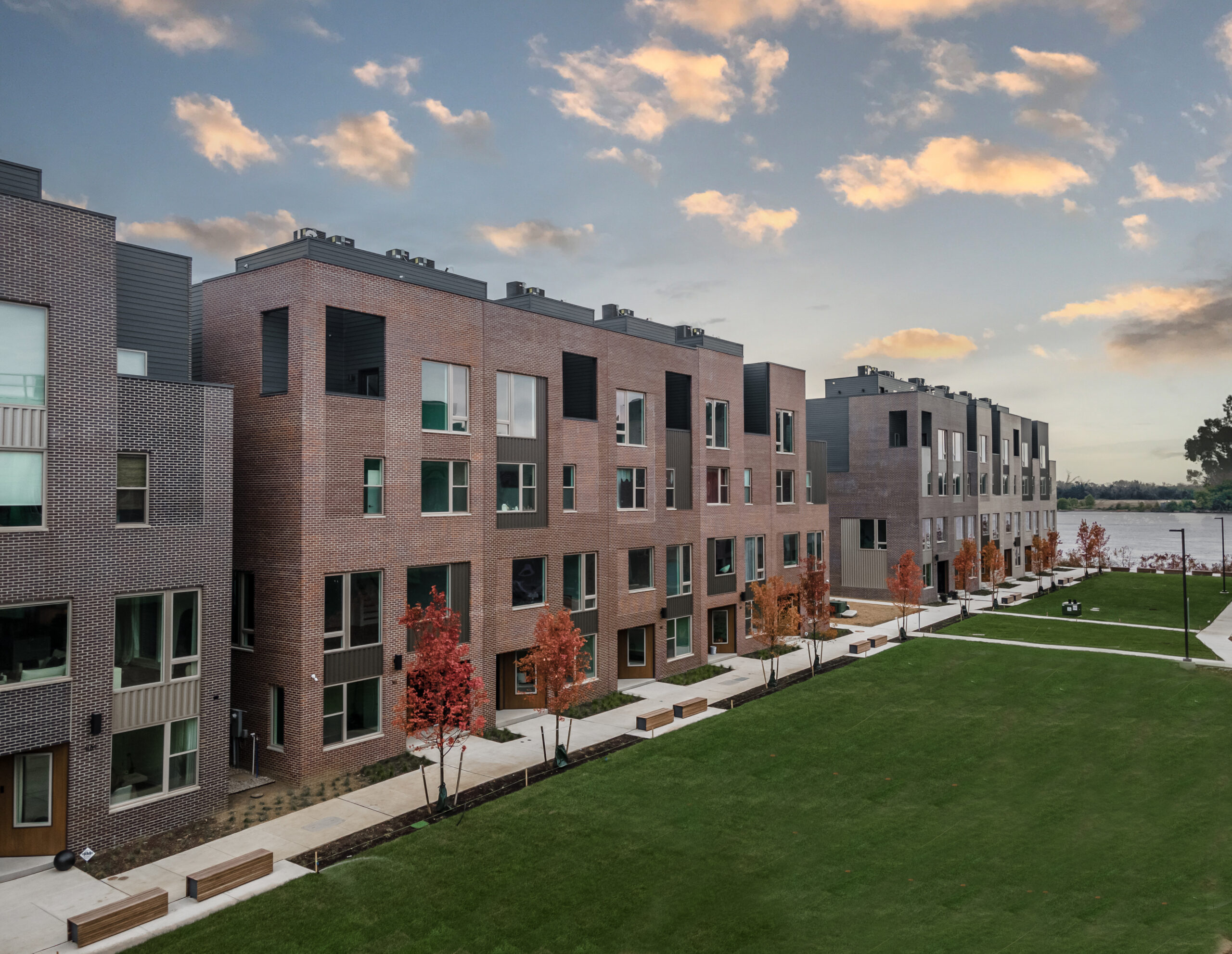 Red brick apartment buildings with sidewalk and green lawn in front and blue sky behind