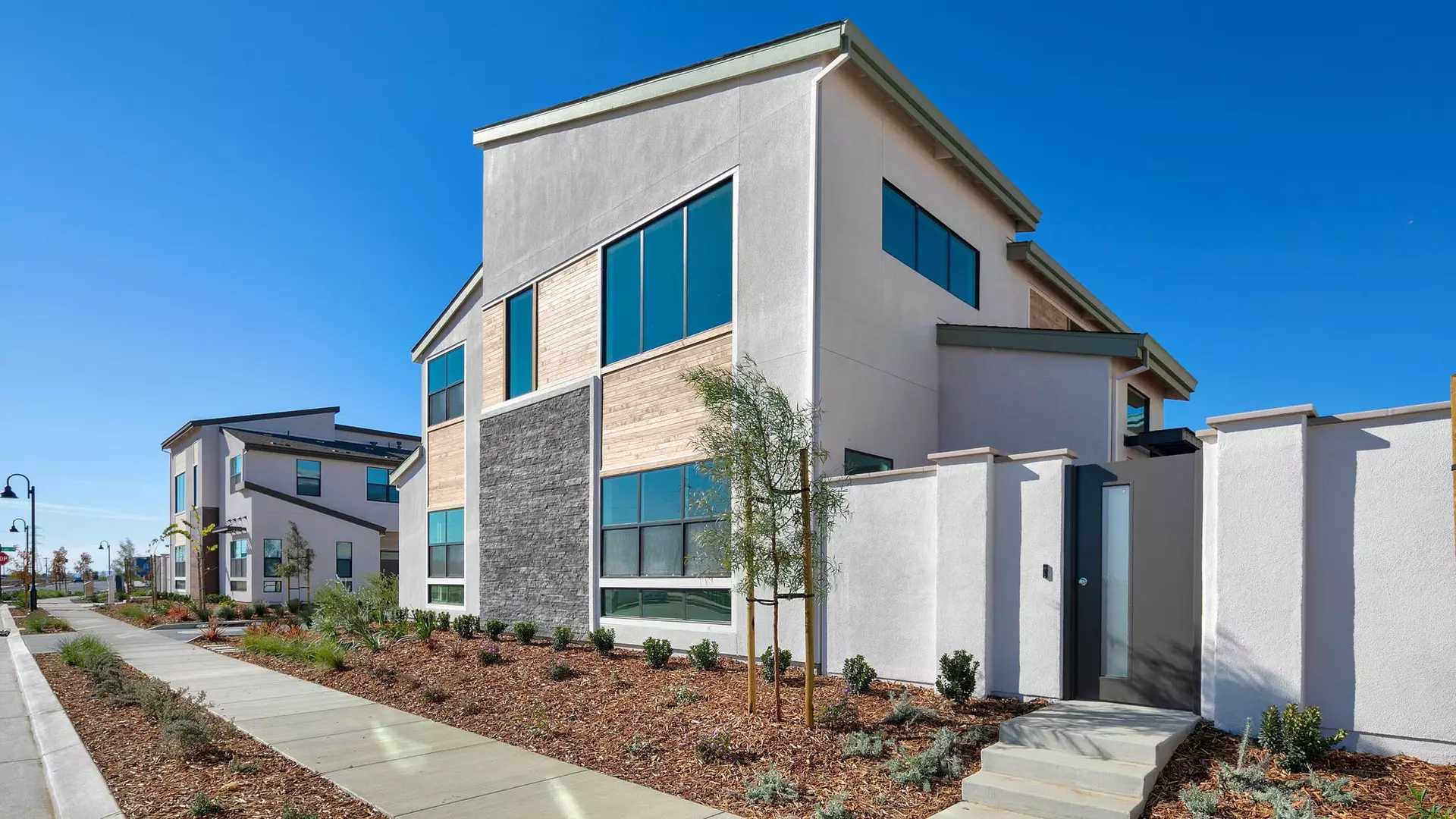 Gray townhome with wooden and stone accents with concrete steps up to door and mulch landscaping in front