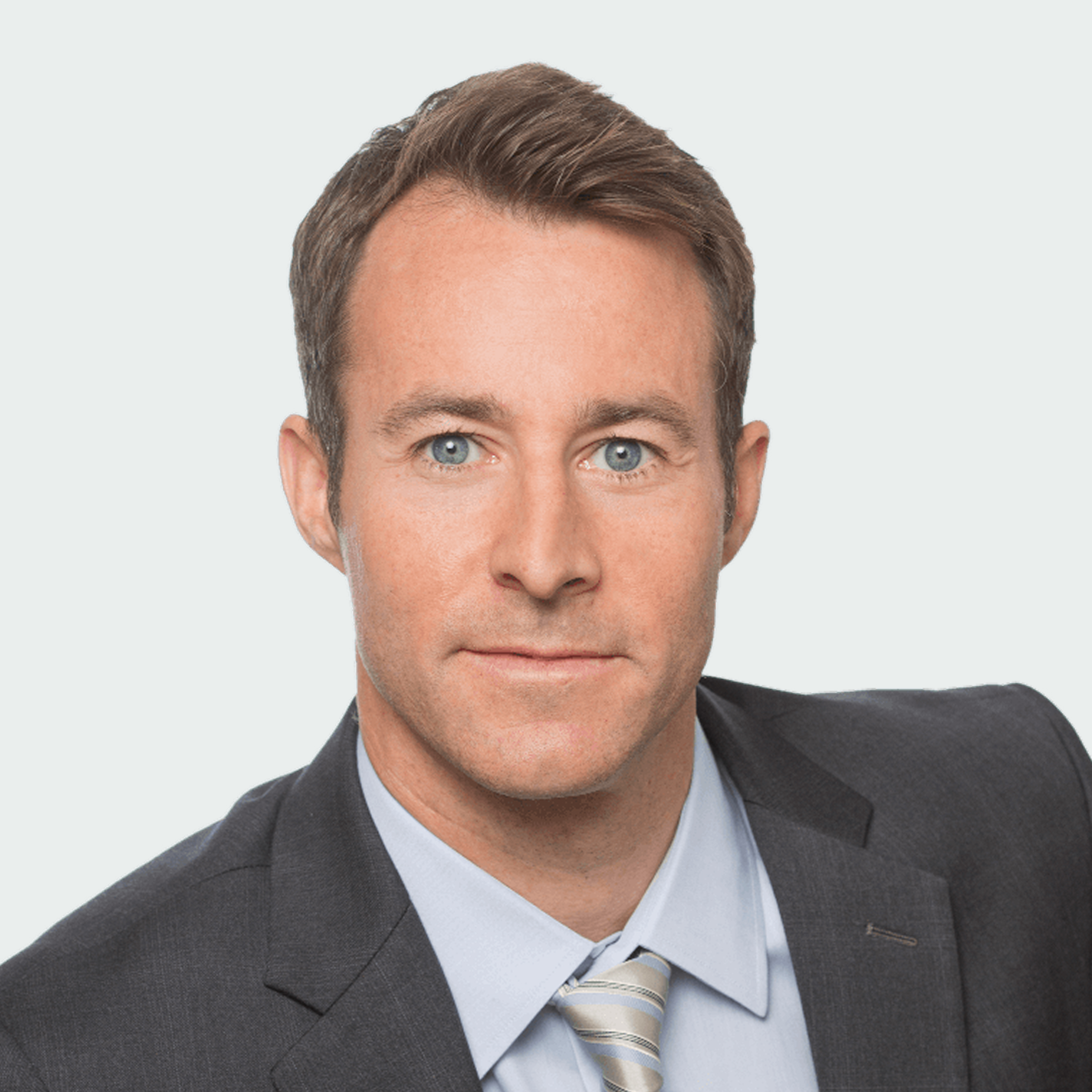A man in a gray suit, light blue shirt, and striped tie looks directly at the camera against a plain light background.