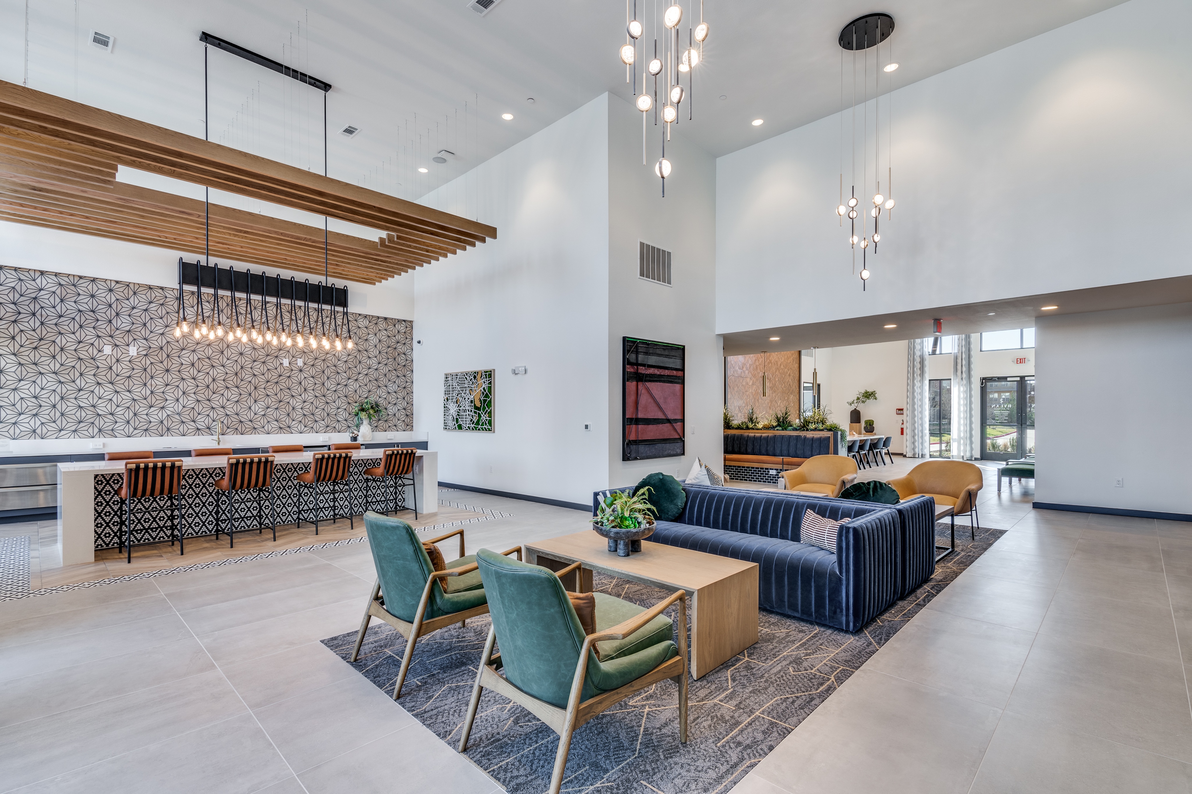Spacious modern lounge with high ceilings, pendant lights, a long dining table, armchairs, sofas, and large windows letting in natural light.