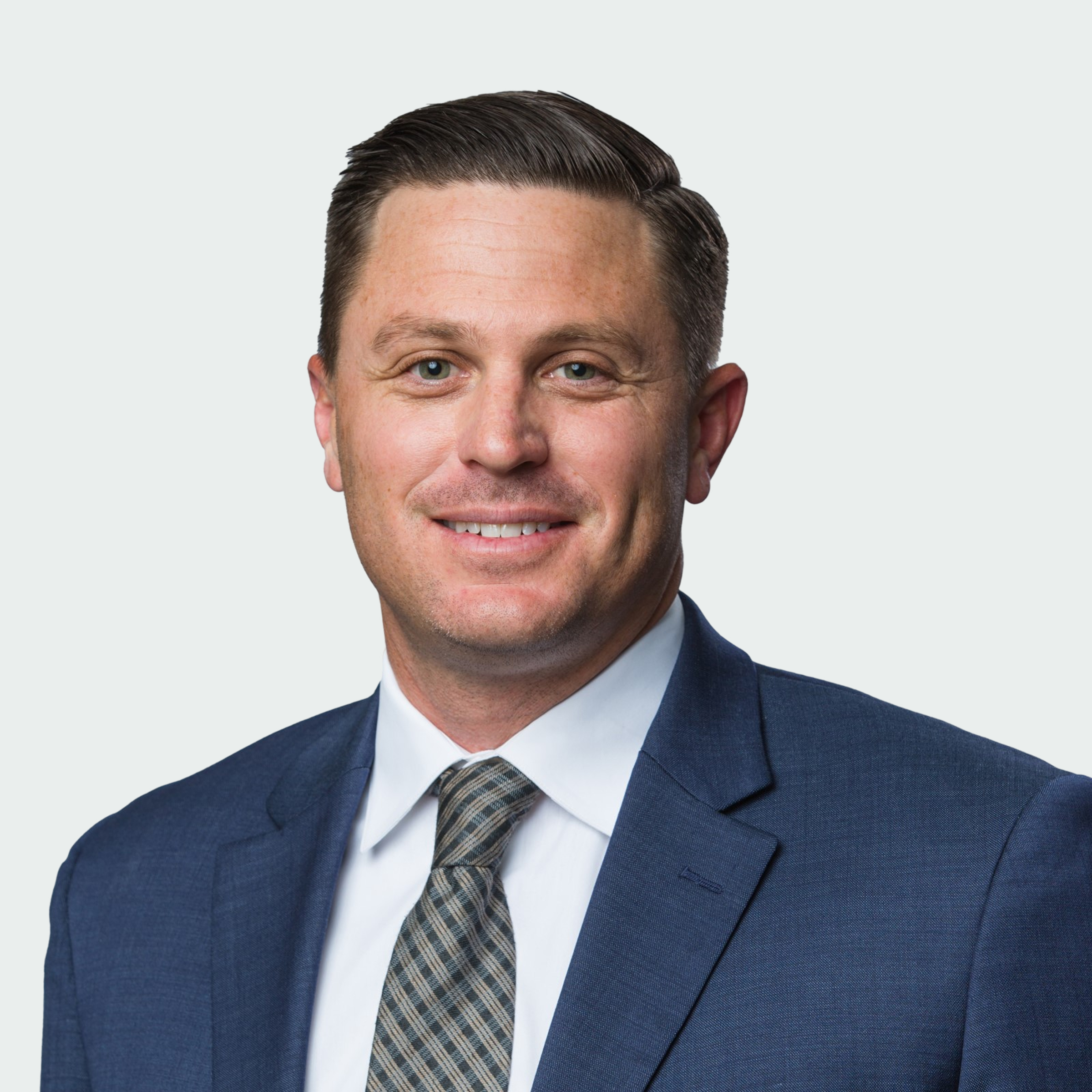 A man in a blue suit, white shirt, and patterned tie smiles at the camera against a plain light background.