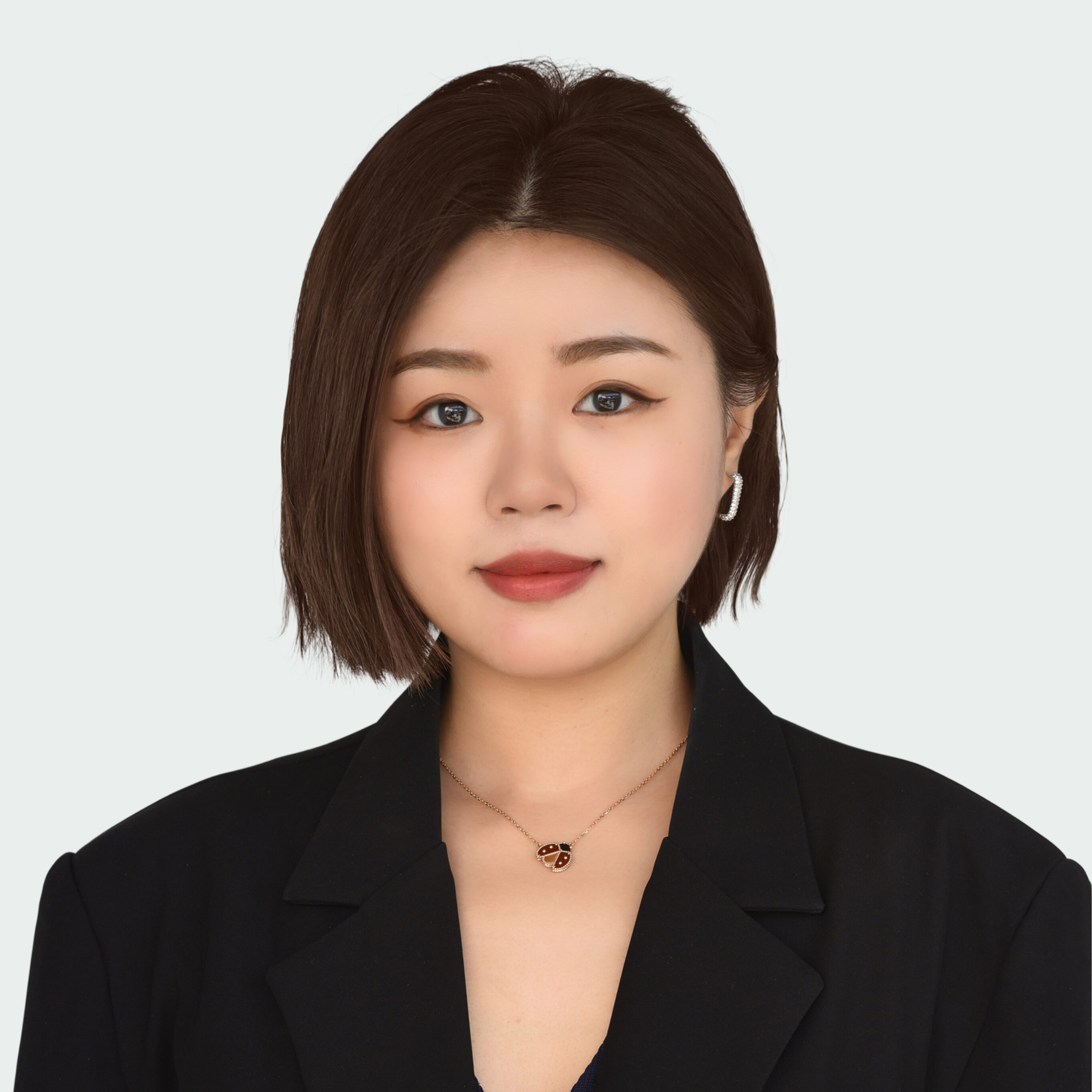 A woman with straight, chin-length dark hair, wearing a black blazer, earrings, and a necklace, poses against a plain white background.