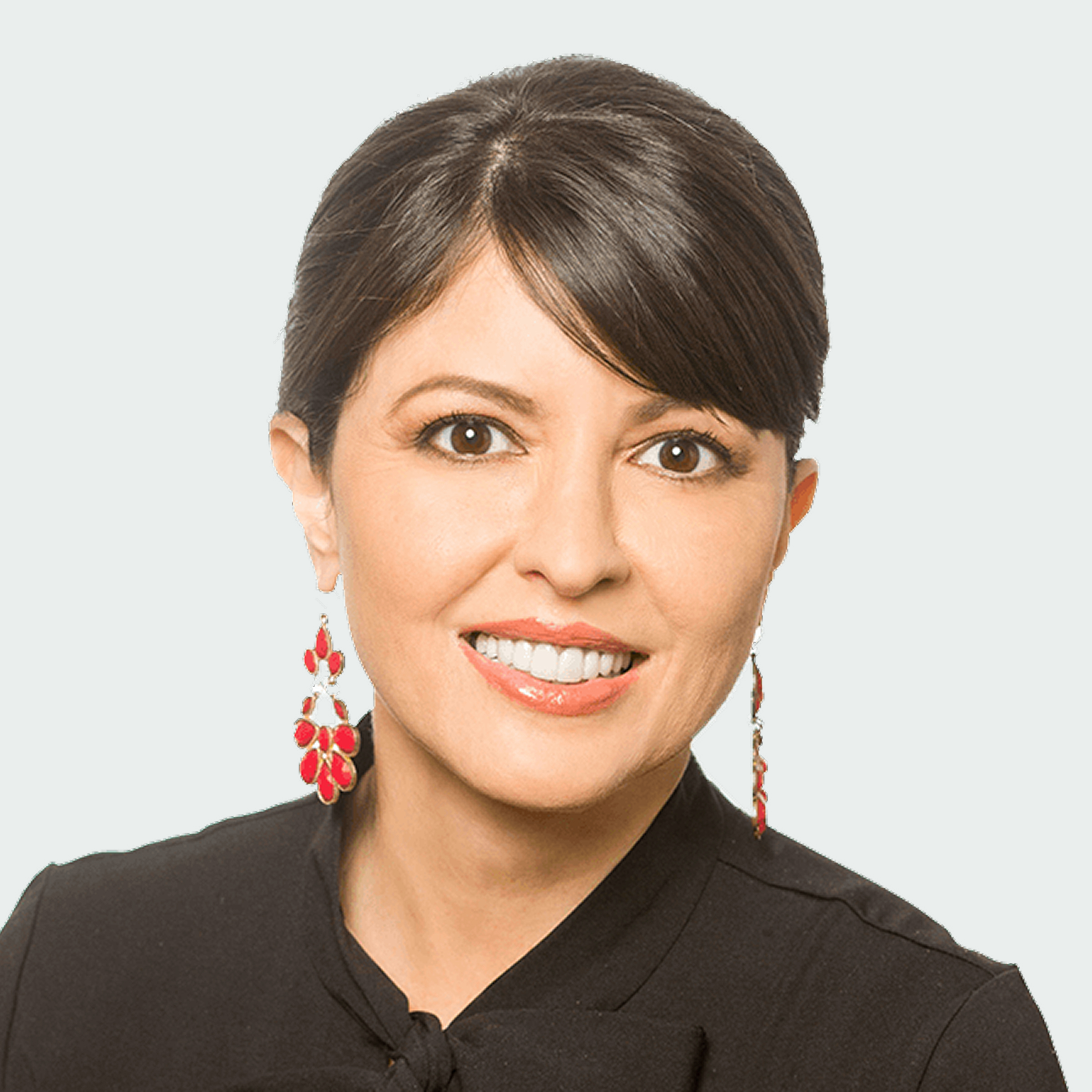 A woman with dark hair in a neat bun, wearing red dangling earrings and a black top, smiling at the camera against a light background.