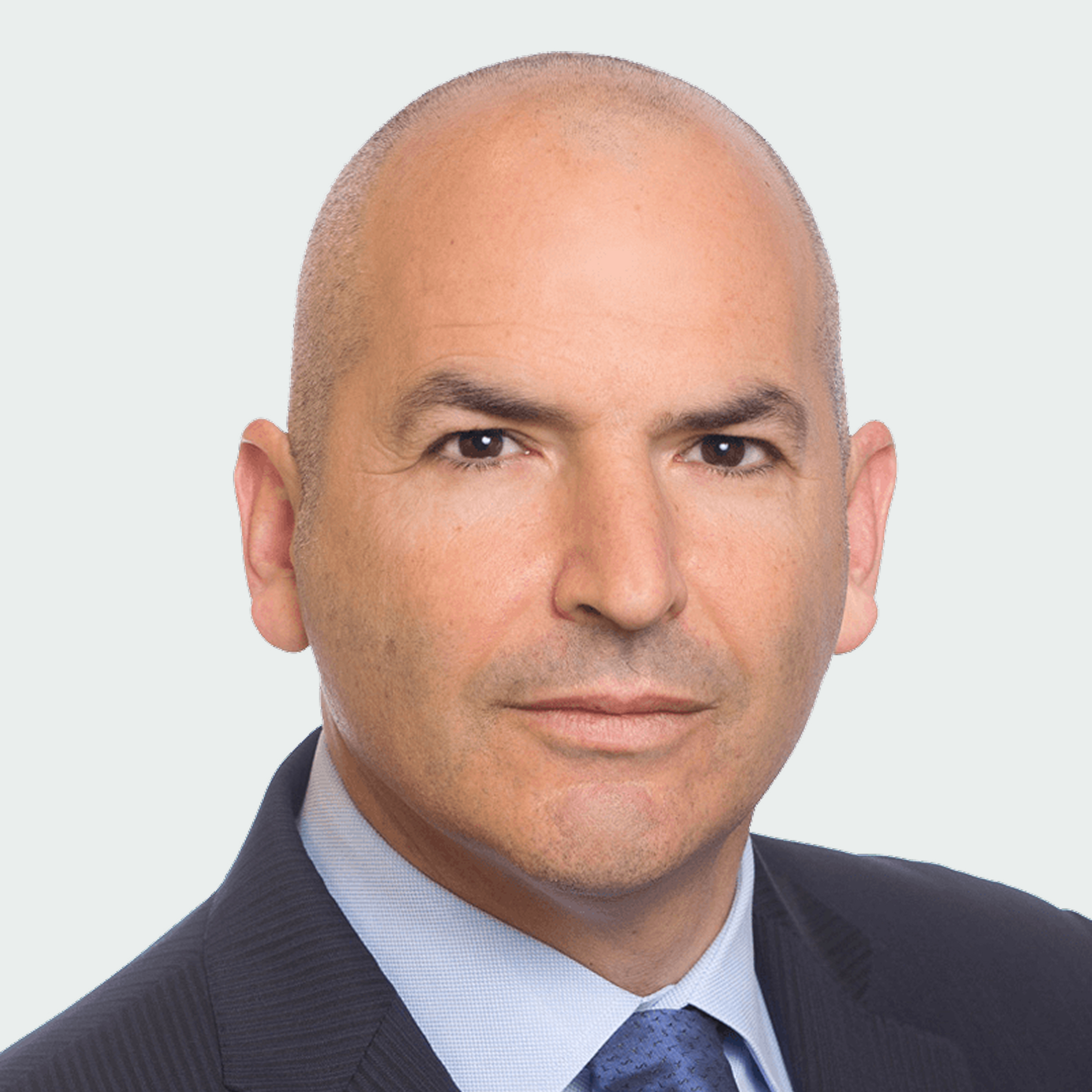 A middle-aged man with a shaved head wearing a dark suit, light blue shirt, and blue tie, looking directly at the camera with a neutral expression.