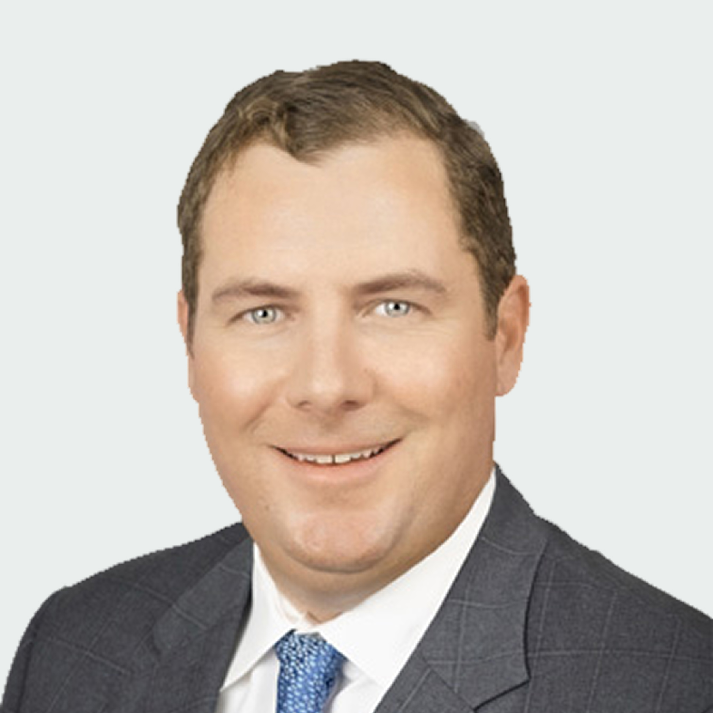 A man with short brown hair wearing a gray suit, white dress shirt, and blue tie, smiling at the camera against a plain light background.