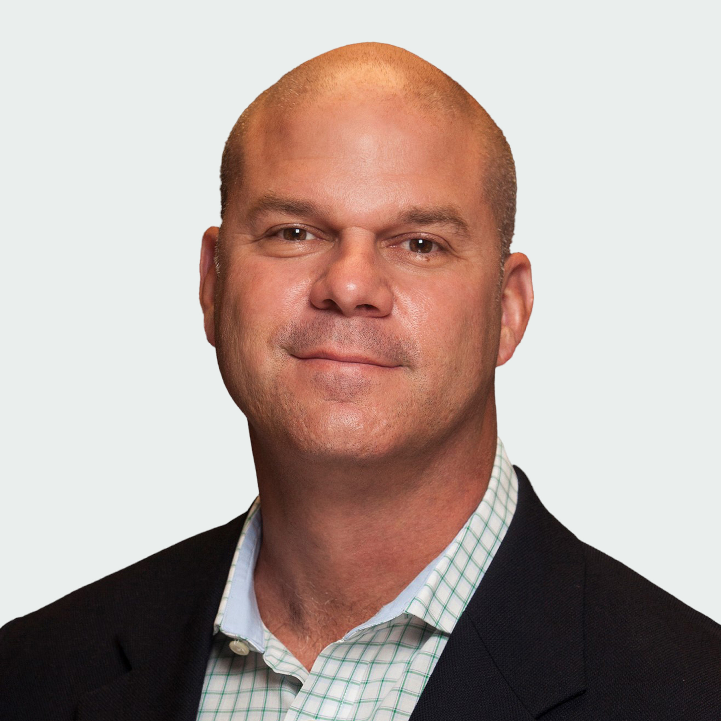 A middle-aged man with a shaved head wearing a dark blazer and a light checkered shirt poses against a plain background.