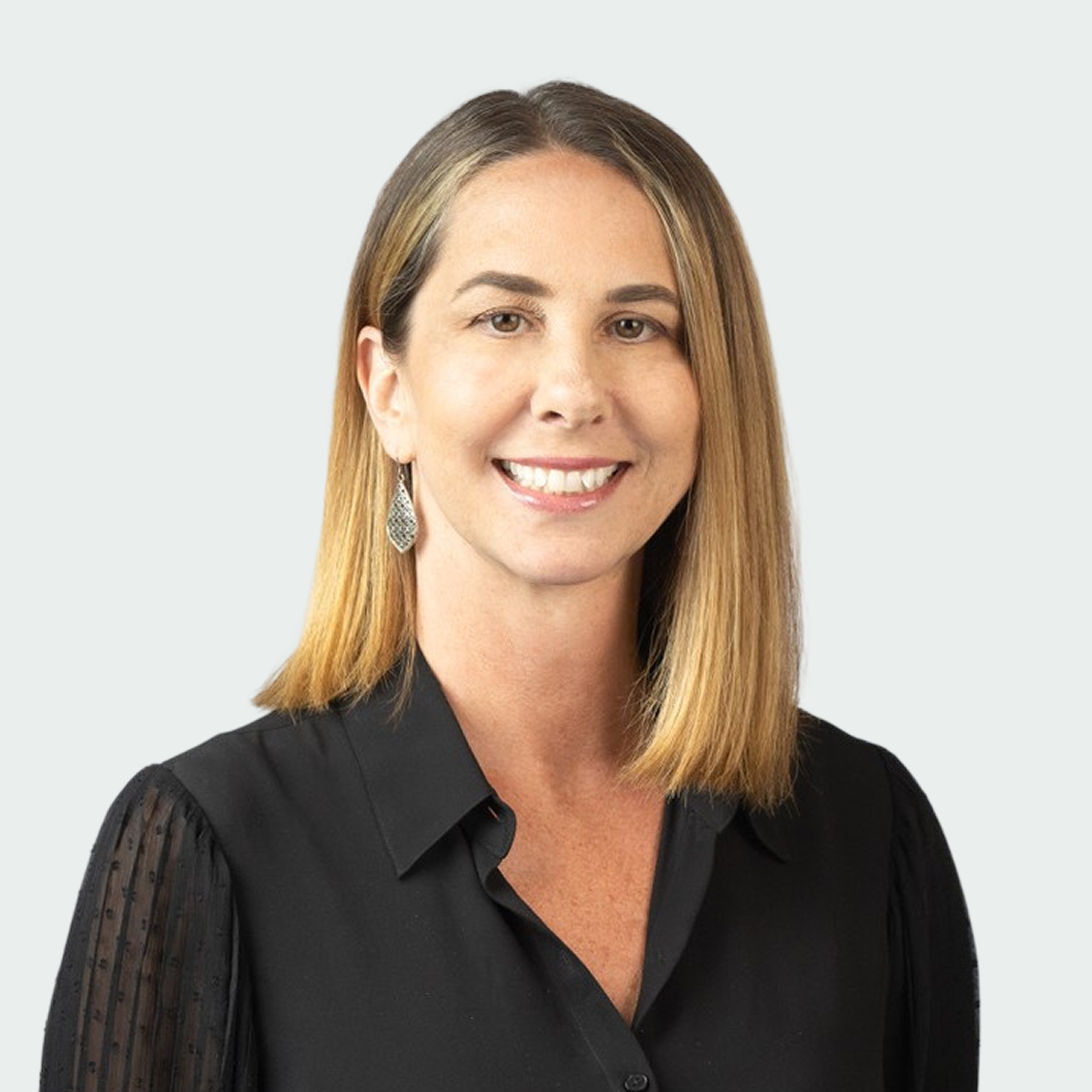 Woman with straight, shoulder-length blonde hair wearing a black blouse and dangling earring, smiling at the camera against a light gray background.